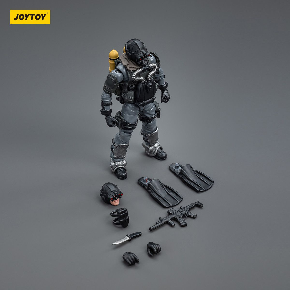 Toy figure of a character in tactical gear with accessories on a gray background, featuring the JOYTOY brand.