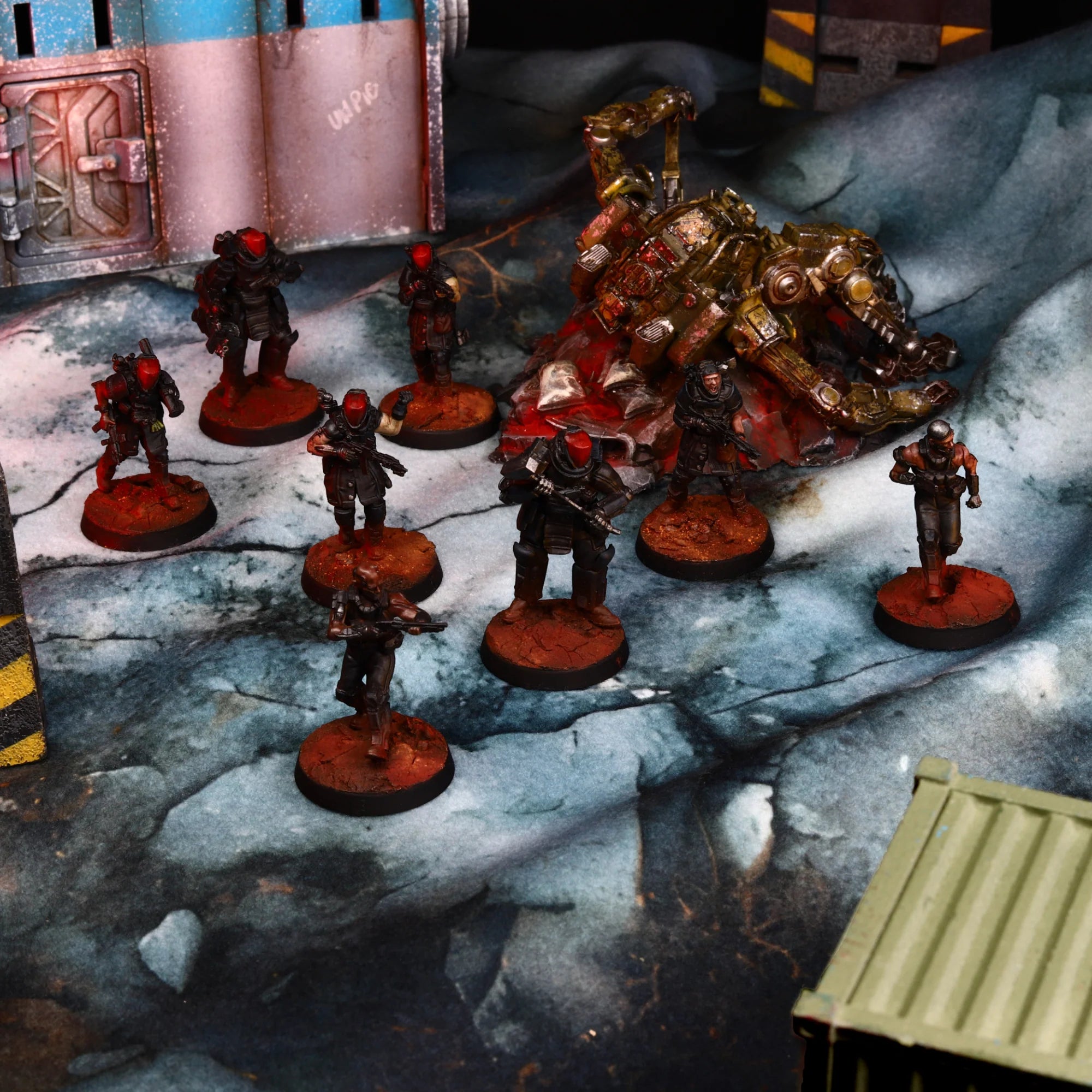 Painted tabletop miniature figures and a large armored monster on a printed sci-fi battle mat with industrial backdrop elements.