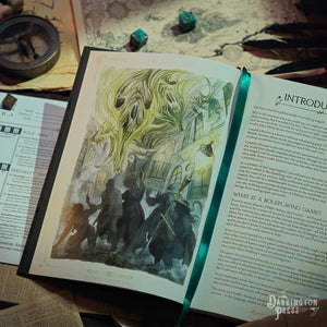 Open book with fantasy illustration and text on a table with gaming supplies